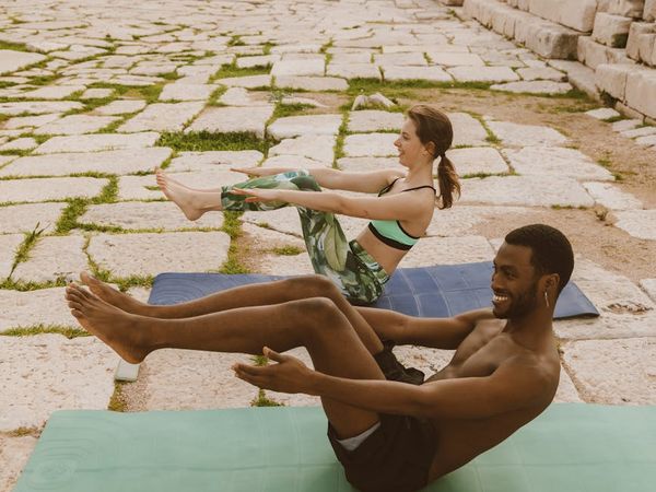 Smiling woman stretching gently on a yoga mat outdoors.